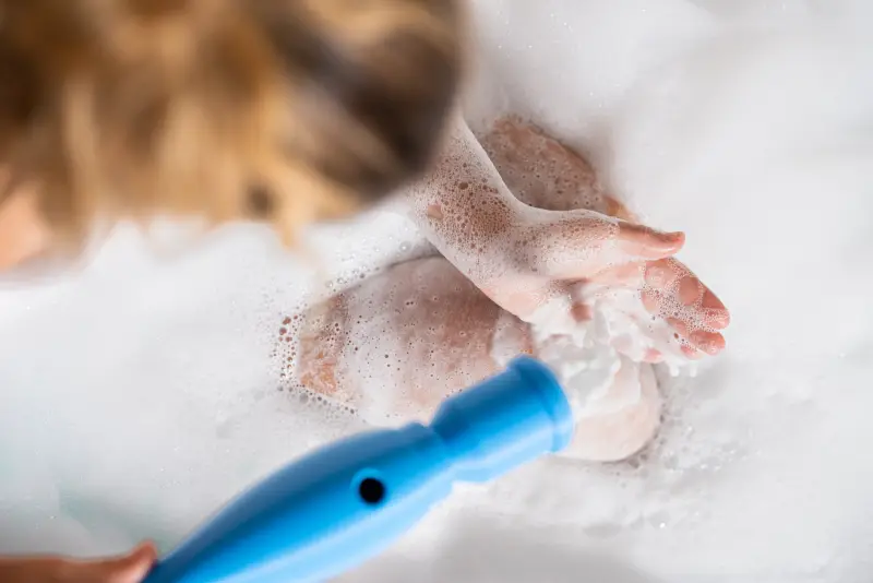 Der blaue SchaumPo-Prototyp liegt im Schaum, eine Hand greift in den Schaum.